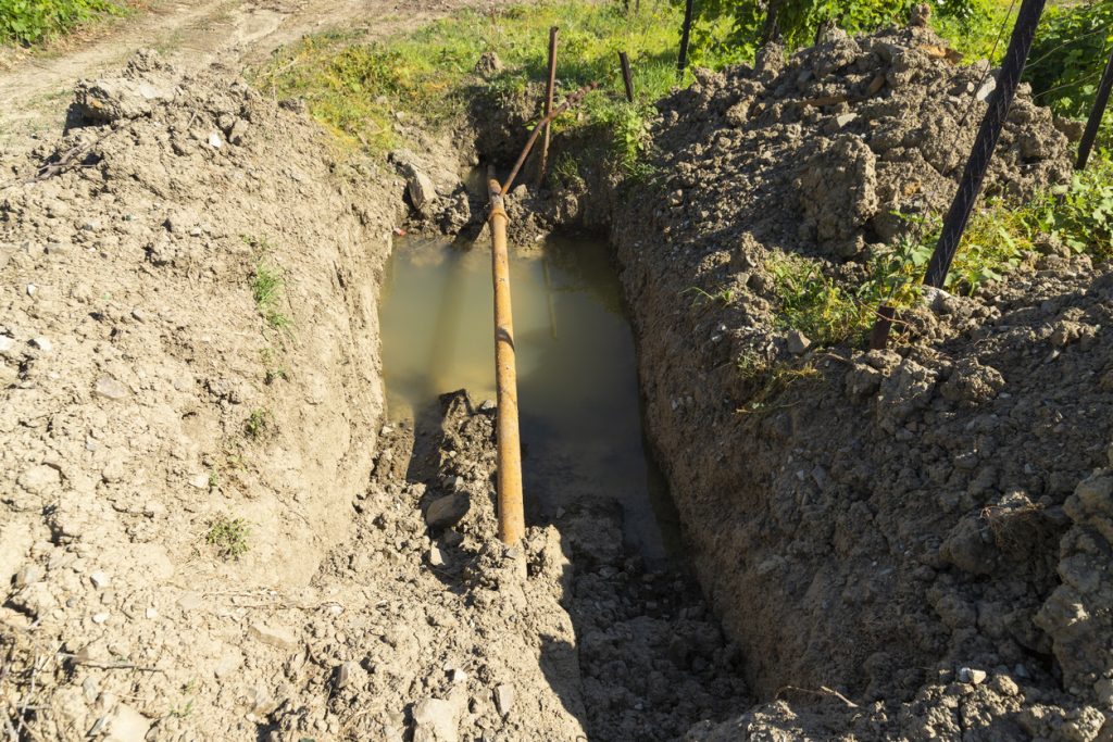 Old rusty metal pipes in a pit with water, water supply system in a mountainous area. Breakthrough of a rusty pipeline.