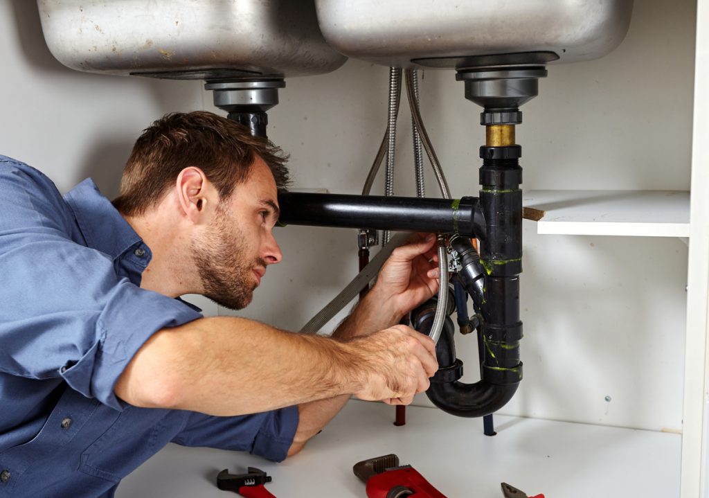 Plumber with tools doing reparation in the kitchen.